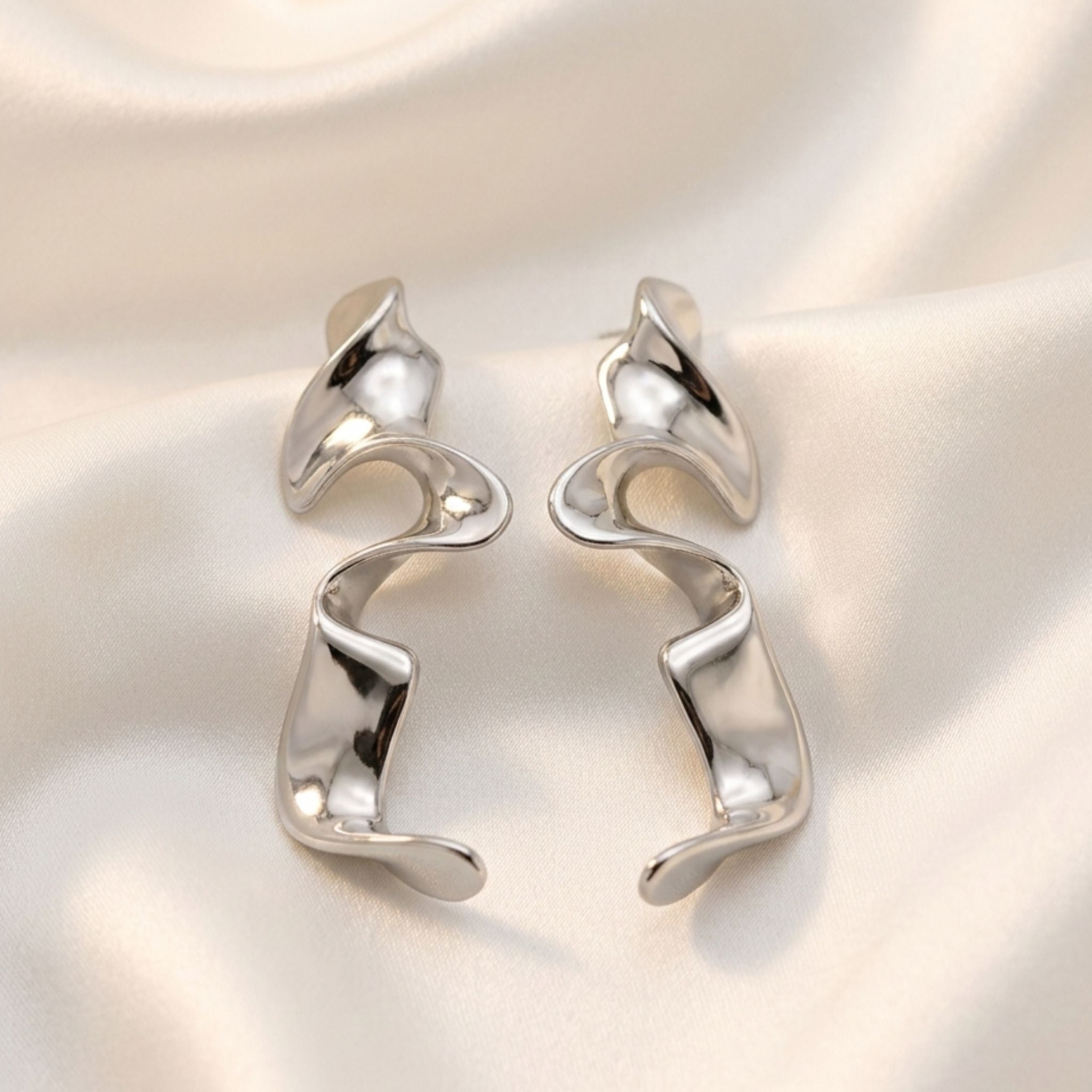 Boucles d’oreilles argentées sculpturales au design ondulé moderne.